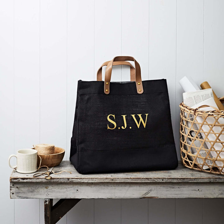 A laminated jute bag with leather handles with initials printed in gold or white.